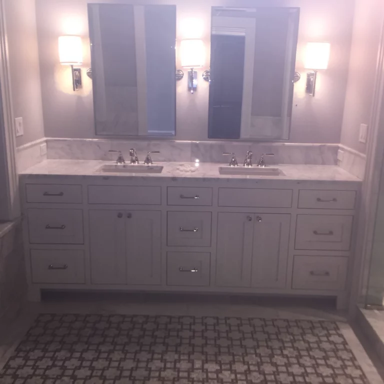 Bathroom remodel with a double-sink vanity, light stone countertop, two mirrors and three wall sconces.