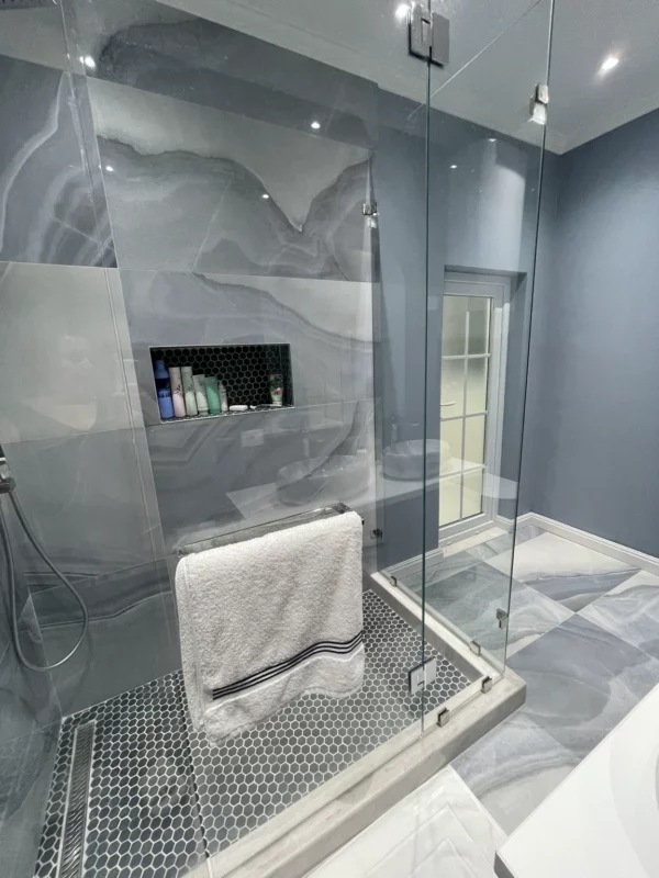 Glass shower enclosure with gray veined tile, a recessed storage niche and a dark mosaic shower floor.