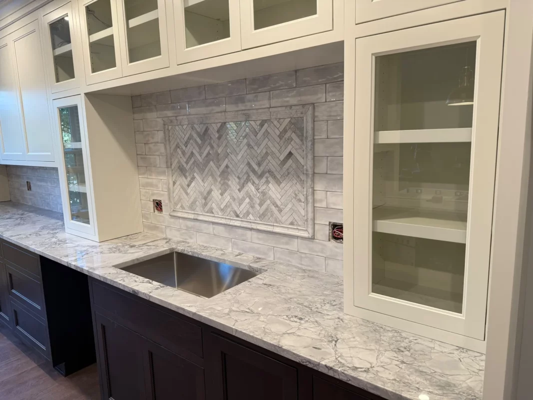 Built-in cabinetry with glass-front doors and a patterned stone backsplash.