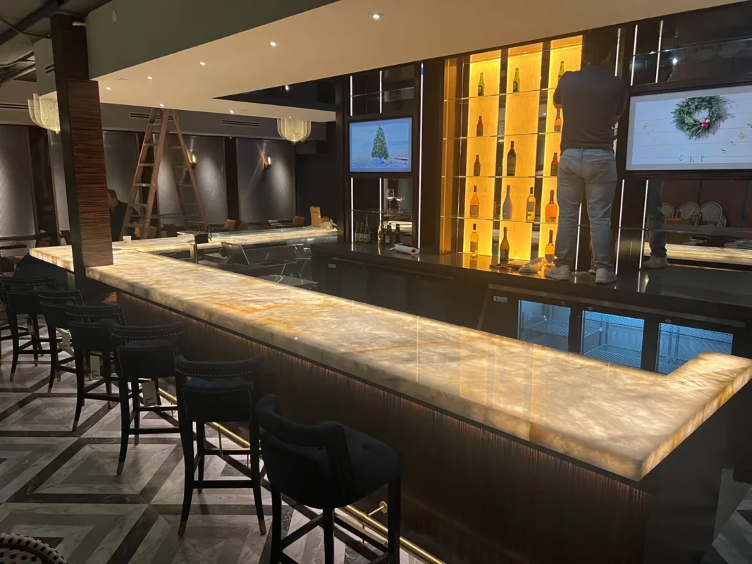 Commercial bar remodel with a long illuminated counter, bar seating and a lit display wall.