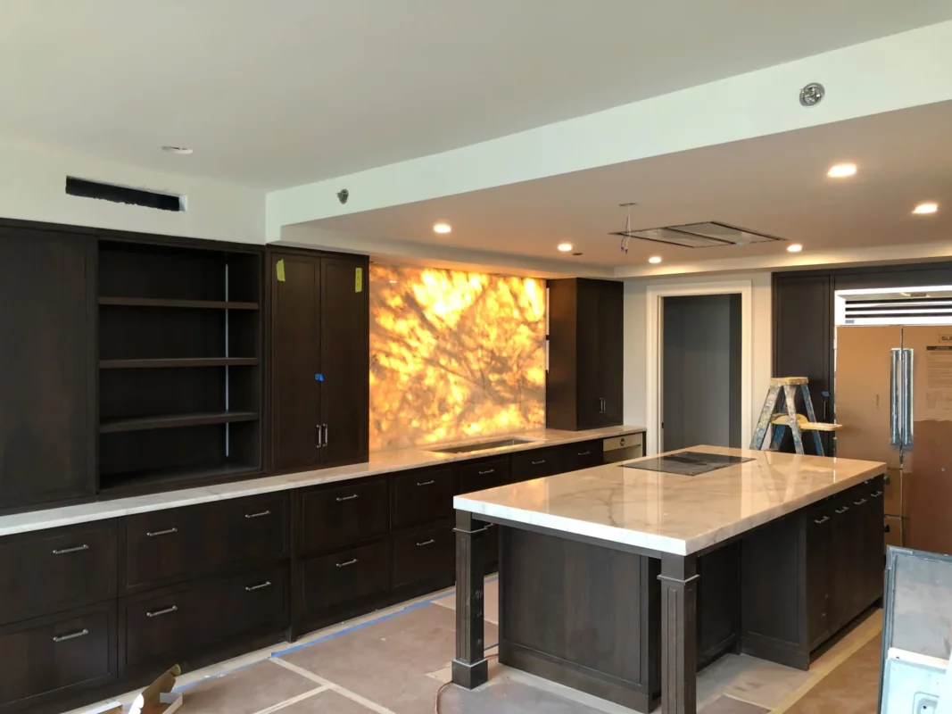 Dark kitchen remodel during installation, featuring an illuminated stone wall.