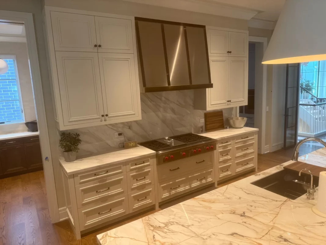 Kitchen remodel with a brass-toned range hood and continuous stone backsplash.