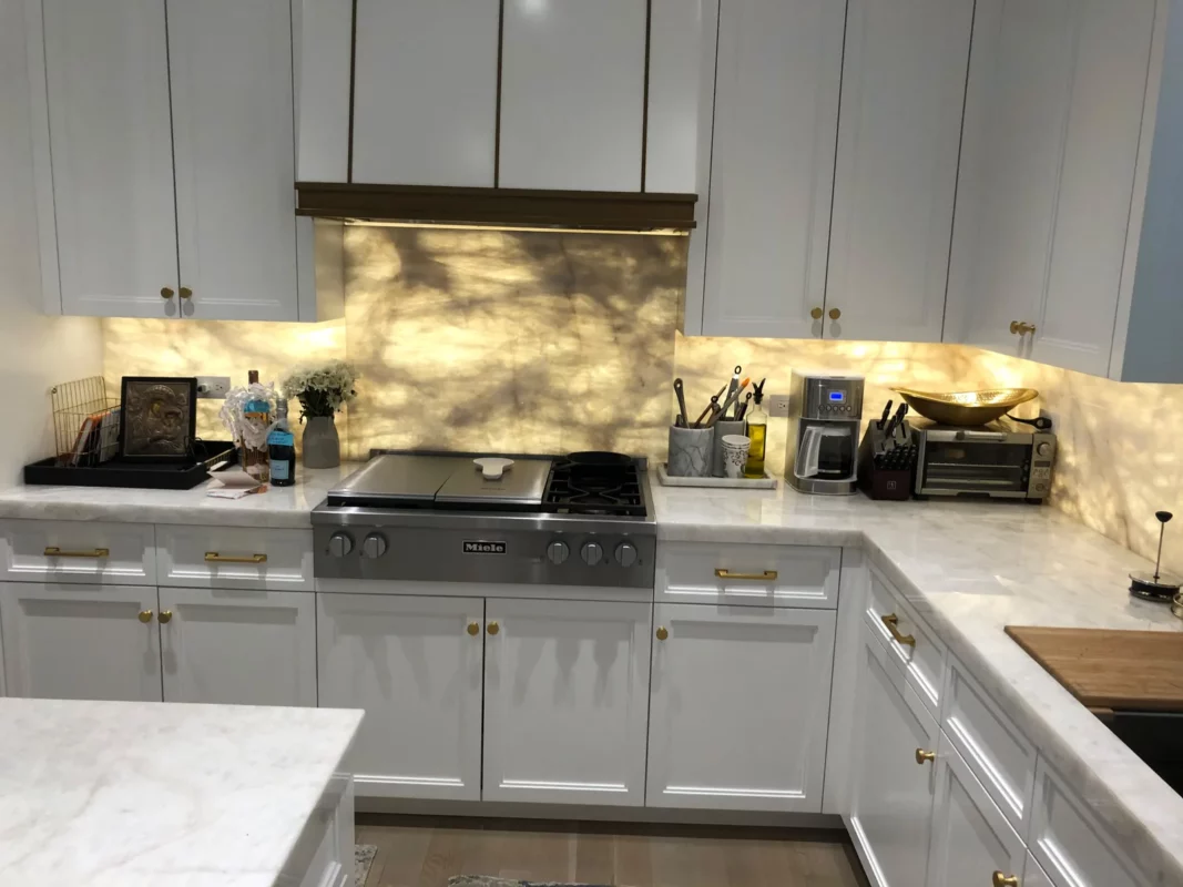 Kitchen remodel with an illuminated stone backsplash and white cabinetry.
