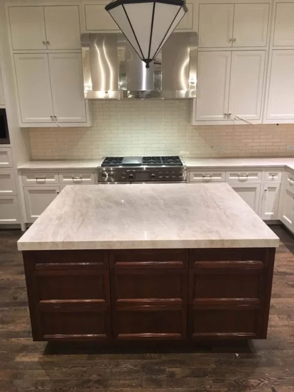 Kitchen remodel with white cabinetry, a dark wood island, light stone countertops and a stainless steel range hood.