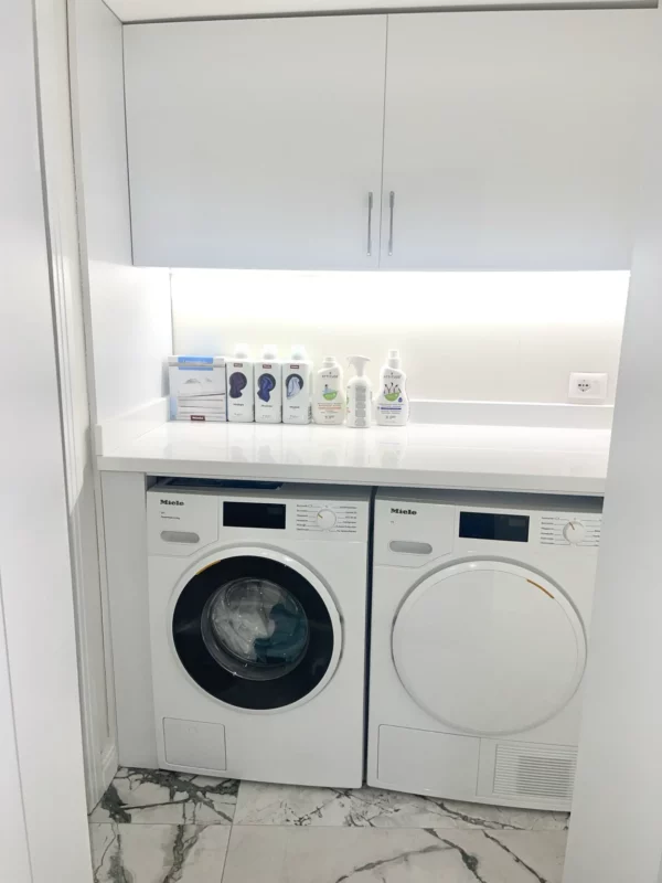 Front-loading washer and dryer beneath a continuous laundry counter, with overhead cabinetry and task lighting.