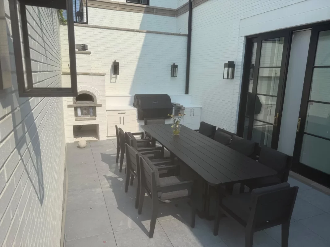 Outdoor dining space with a long table, built-in grill and fireplace.