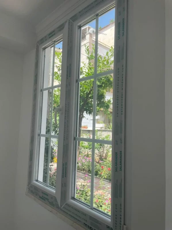 Replacement window with white frames and divided-light glazing; protective frame film remains during installation.