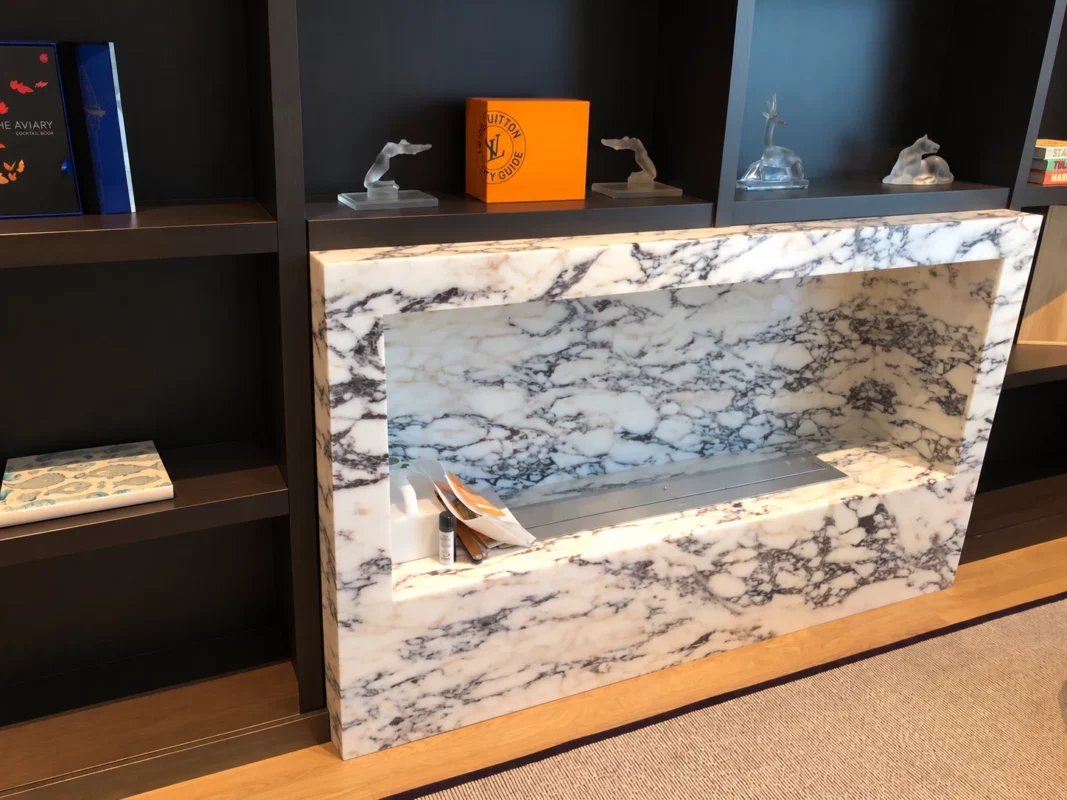 Veined stone fireplace surround and metal burner set within dark built-in shelving, photographed during installation.