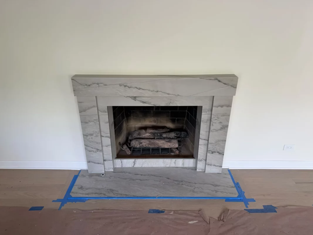 Veined stone fireplace surround during installation; floor protection remains in place.