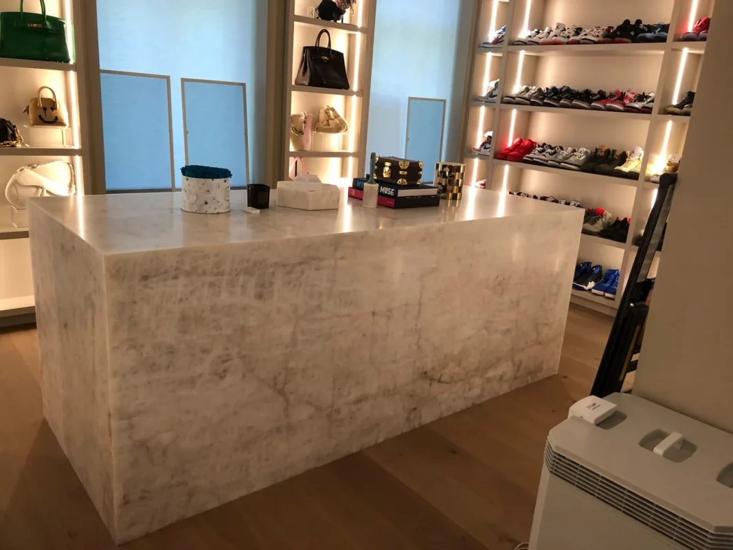 Walk-in closet remodel with a stone island and illuminated shoe and handbag shelving.