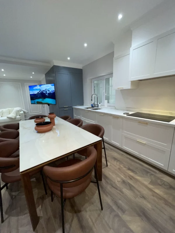 Kitchen remodel with white cabinetry, a tall blue storage unit, gold-toned handles and a dining table with upholstered chairs.