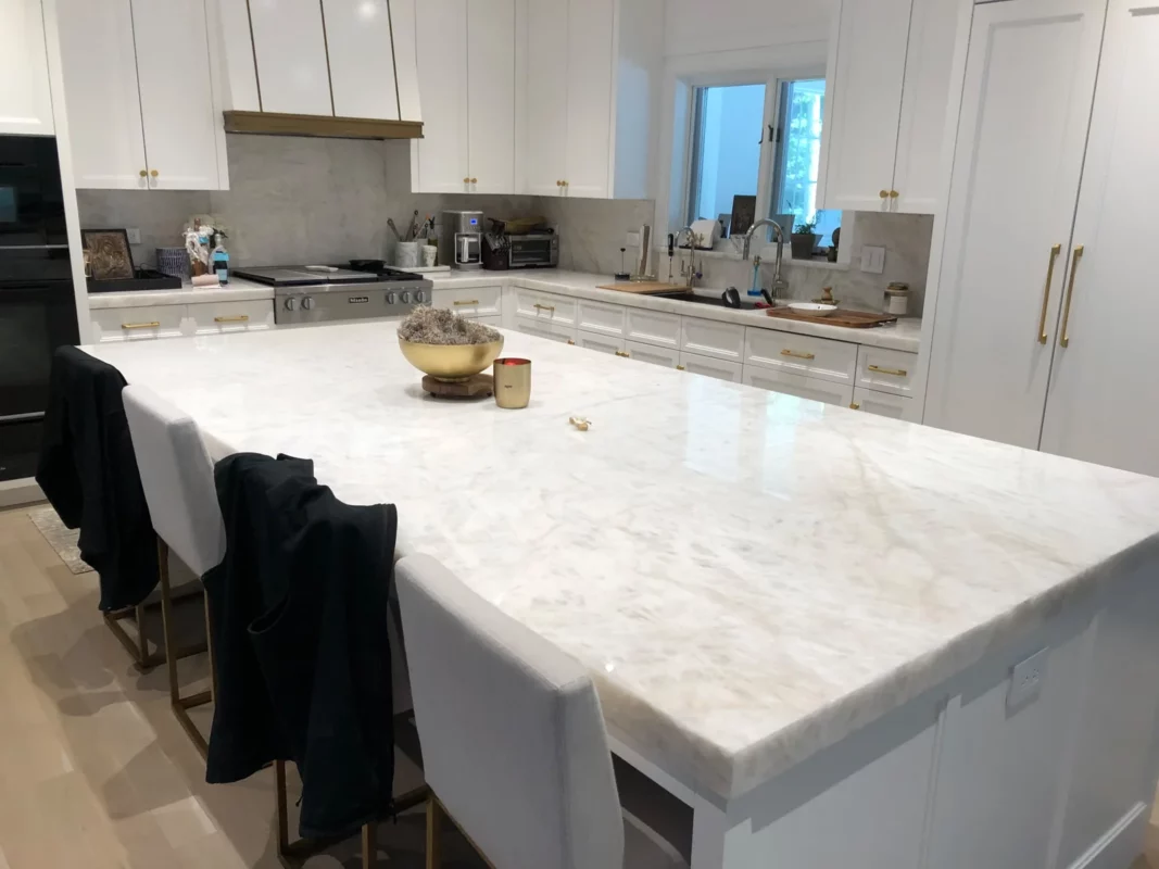 White kitchen remodel with a large stone island and integrated seating.