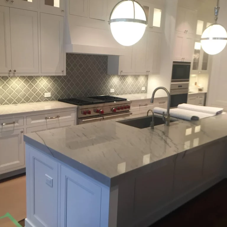 White kitchen remodel with a patterned backsplash, stone island and globe pendant lighting.