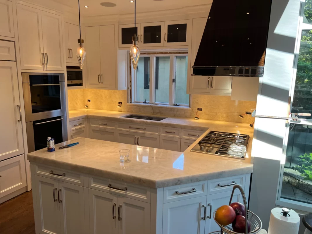 White kitchen remodel with a stone island and contrasting range hood.