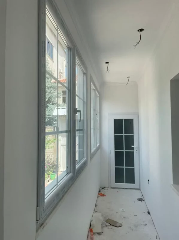 A row of replacement windows and a glazed door along a corridor during renovation, before final cleanup and lighting installation.